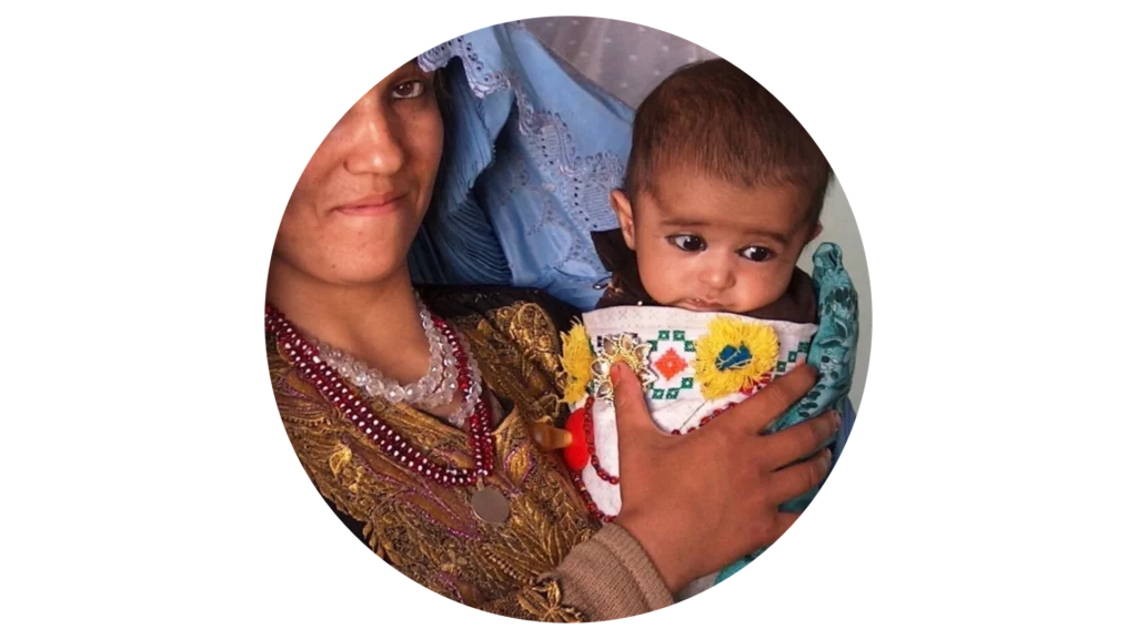 A woman holds a baby wrapped in a colorful blanket.