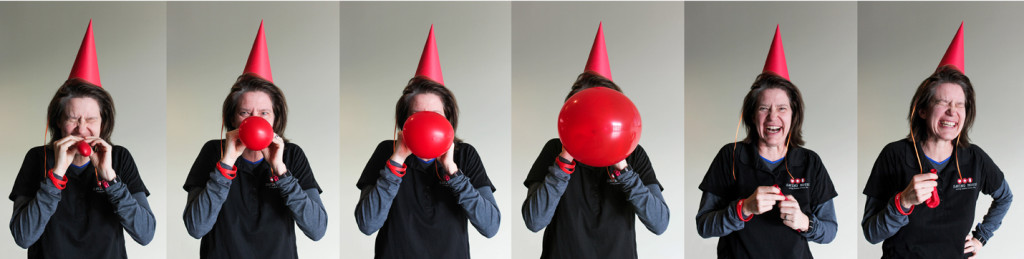 Person wearing a party hat, expressing joy and surprise while interacting with a red balloon, celebrating a birthday for Saving Moses' fifth anniversary.