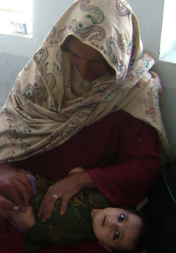 Woman in traditional attire holding a baby, both appearing vulnerable, reflecting the challenges faced by pregnant women in rural Afghanistan seeking medical care.