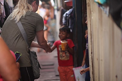 Woman interacting with smiling child in a narrow alley, showcasing community support and care for vulnerable children in a joyful atmosphere.