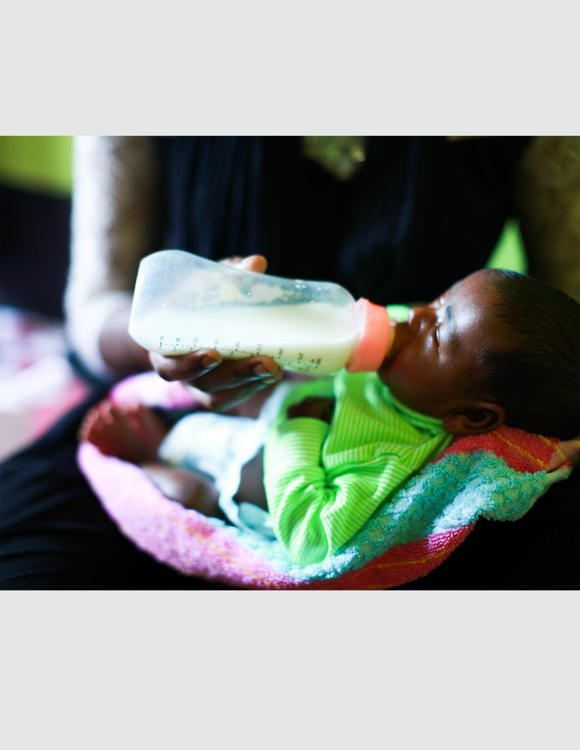 Infant being fed with a milk bottle, wrapped in a colorful blanket, highlighting child care initiatives by Saving Moses.