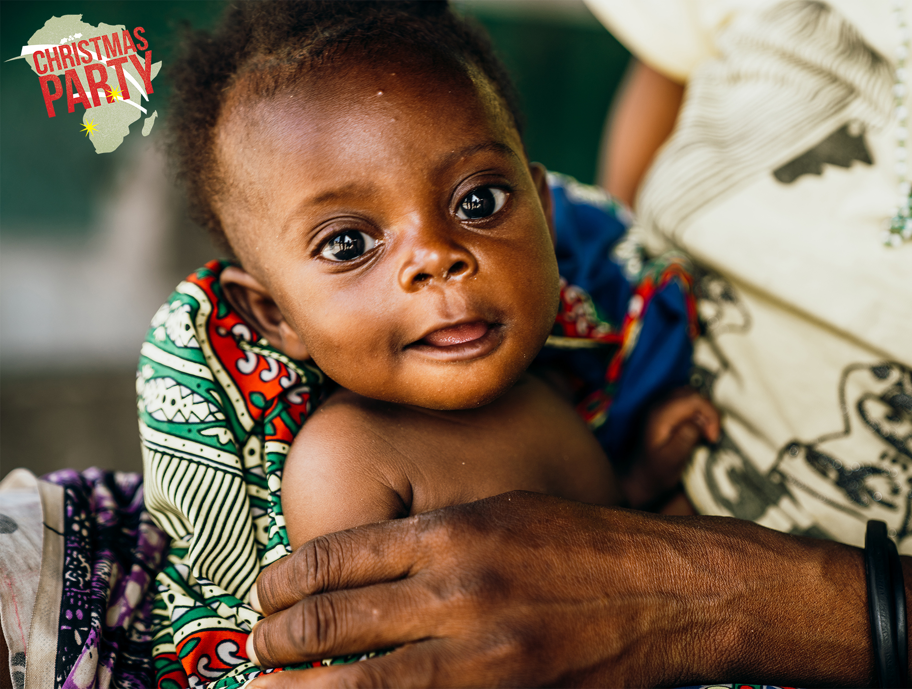 Infant with expressive eyes wrapped in colorful fabric, symbolizing the joy and hope of vulnerable children supported by Saving Moses during festive events.