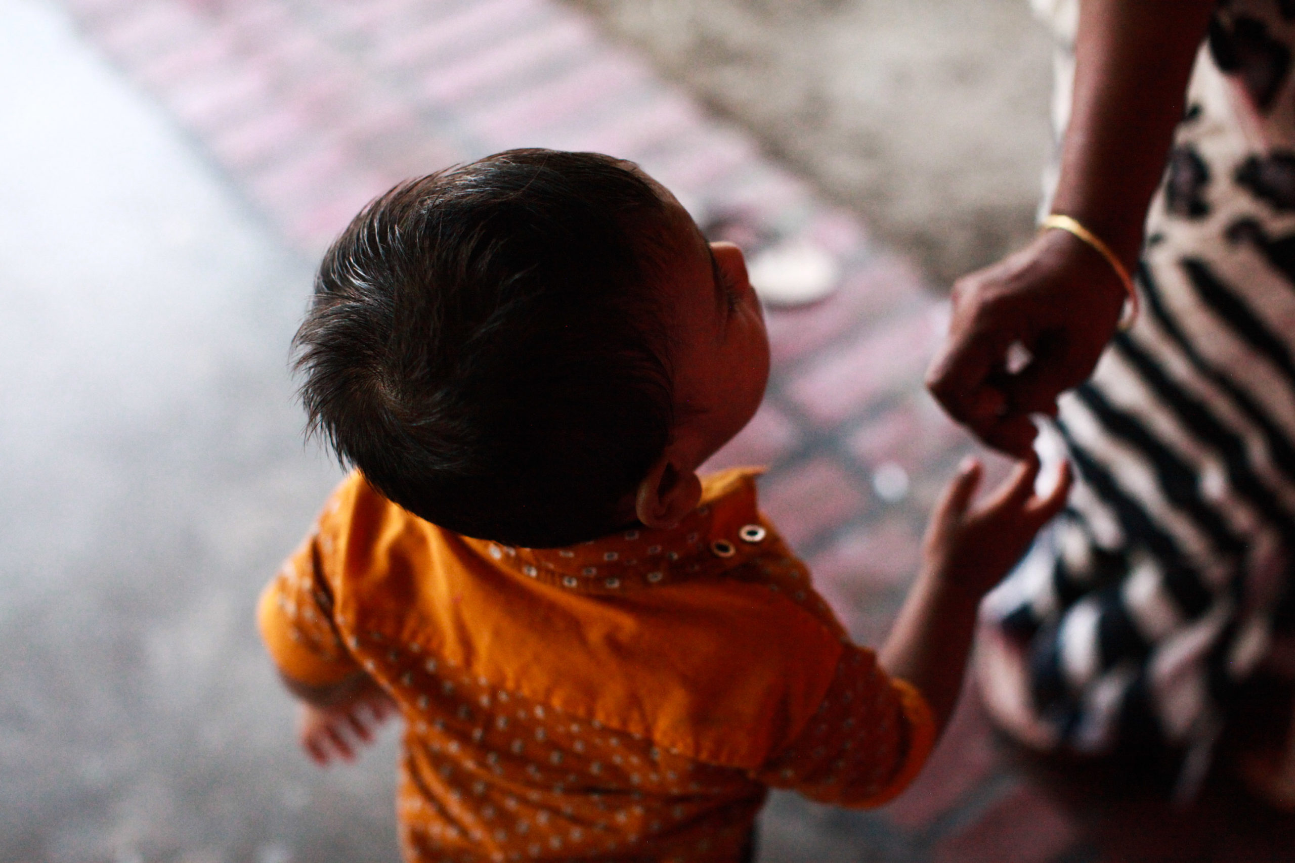 Child in orange shirt reaching for a hand, highlighting vulnerability and connection in a Bangladesh setting related to the NightCare program for children of sex workers.