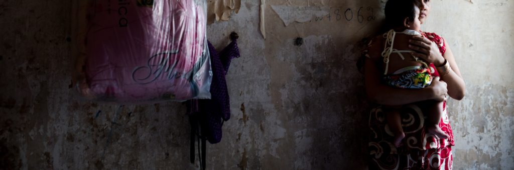 Mother holding baby in a dimly lit room, showcasing vulnerability and care amidst challenging circumstances, reflecting themes of motherhood and survival related to the NightCare program by Saving Moses.