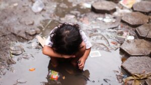 Surviving the Underpass - a little girl in Cambodia standing in a mud puddle.