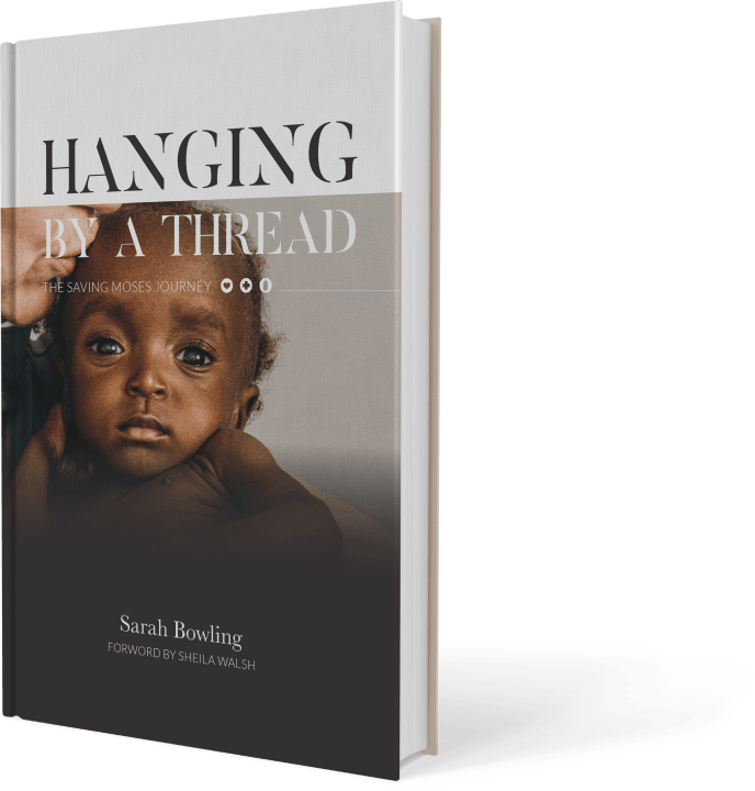 Book cover of "Hanging by a Thread" by Sarah Bowling featuring a close-up of a baby’s face, symbolizing the mission of Saving Moses to aid vulnerable children.