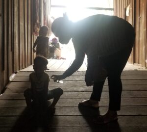 Child sitting on wooden floor with caregiver reaching out, dimly lit environment, emphasizing vulnerability and support during COVID-19 crisis.