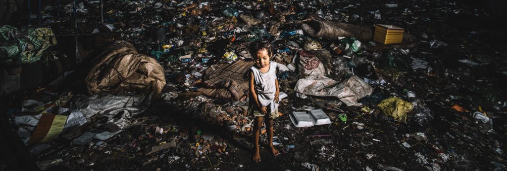 A little toddler girl standing in a pile of garbage.