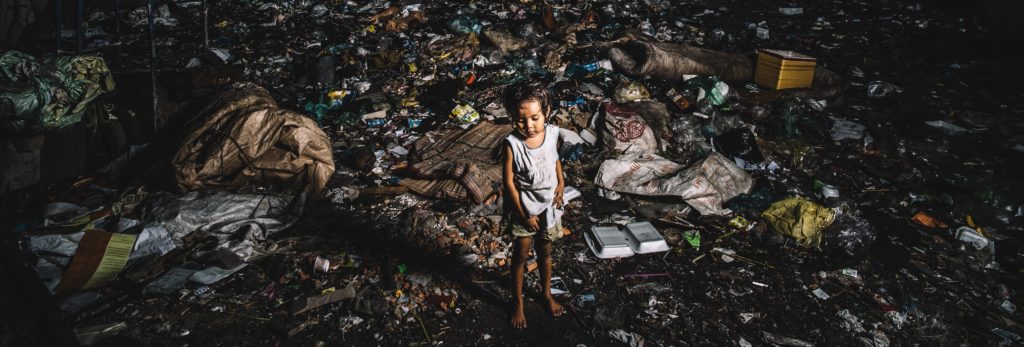 Child standing amidst litter and debris in a neglected environment, highlighting the urgent need for child welfare and protection rights.
