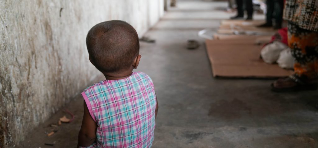 Child sitting on the floor, back view, in a dimly lit environment, symbolizing vulnerability and neglect, relevant to Saving Moses' mission to protect children of sex workers.