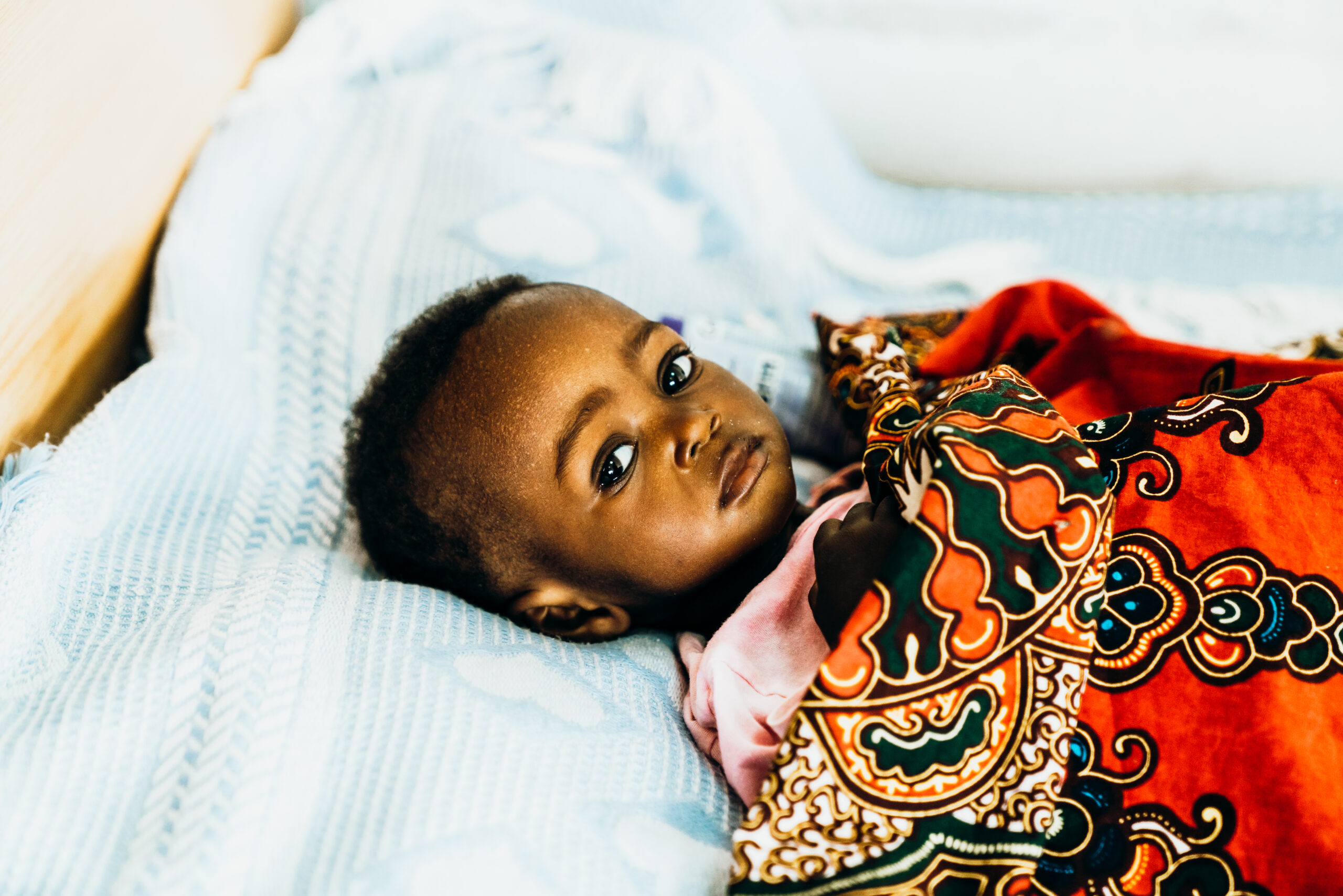 Vulnerable baby lying on a blue blanket, wrapped in a colorful patterned cloth, highlighting the need for safety and healing supported by donations to Saving Moses.