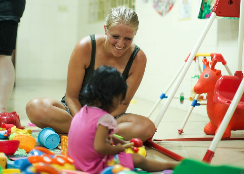 Woman playing with a young girl surrounded by colorful toys in a nurturing environment, highlighting child welfare and humanitarian aid efforts.