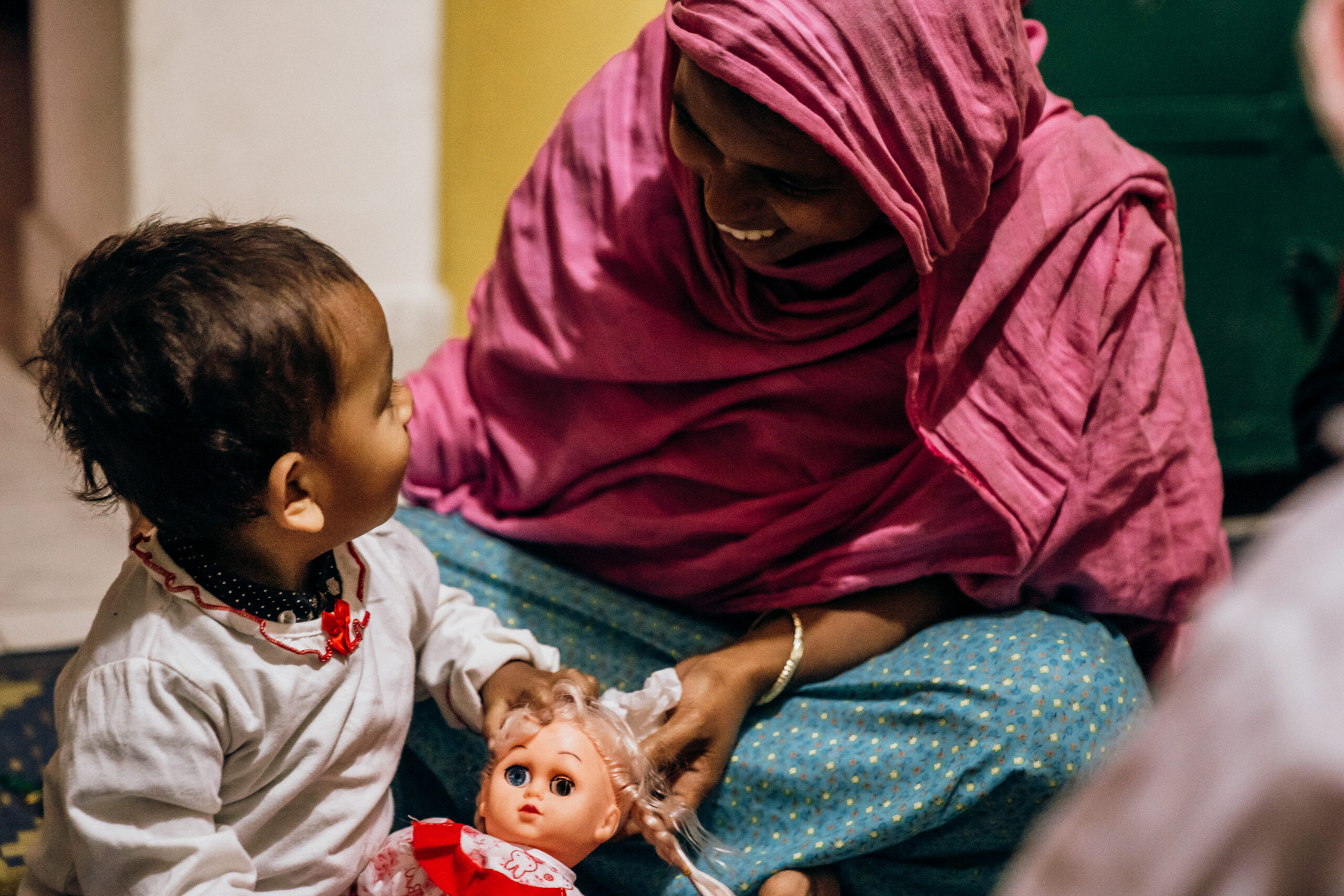 Mother and child interacting, child holding a doll, both smiling, in a nurturing environment, emphasizing the importance of care and support for vulnerable babies as promoted by Saving Moses.