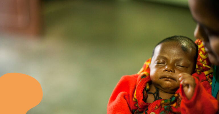 MicrosoftTeams-image (1) Infant in red blanket being cradled, representing vulnerable babies in India supported by Saving Moses during the pandemic.