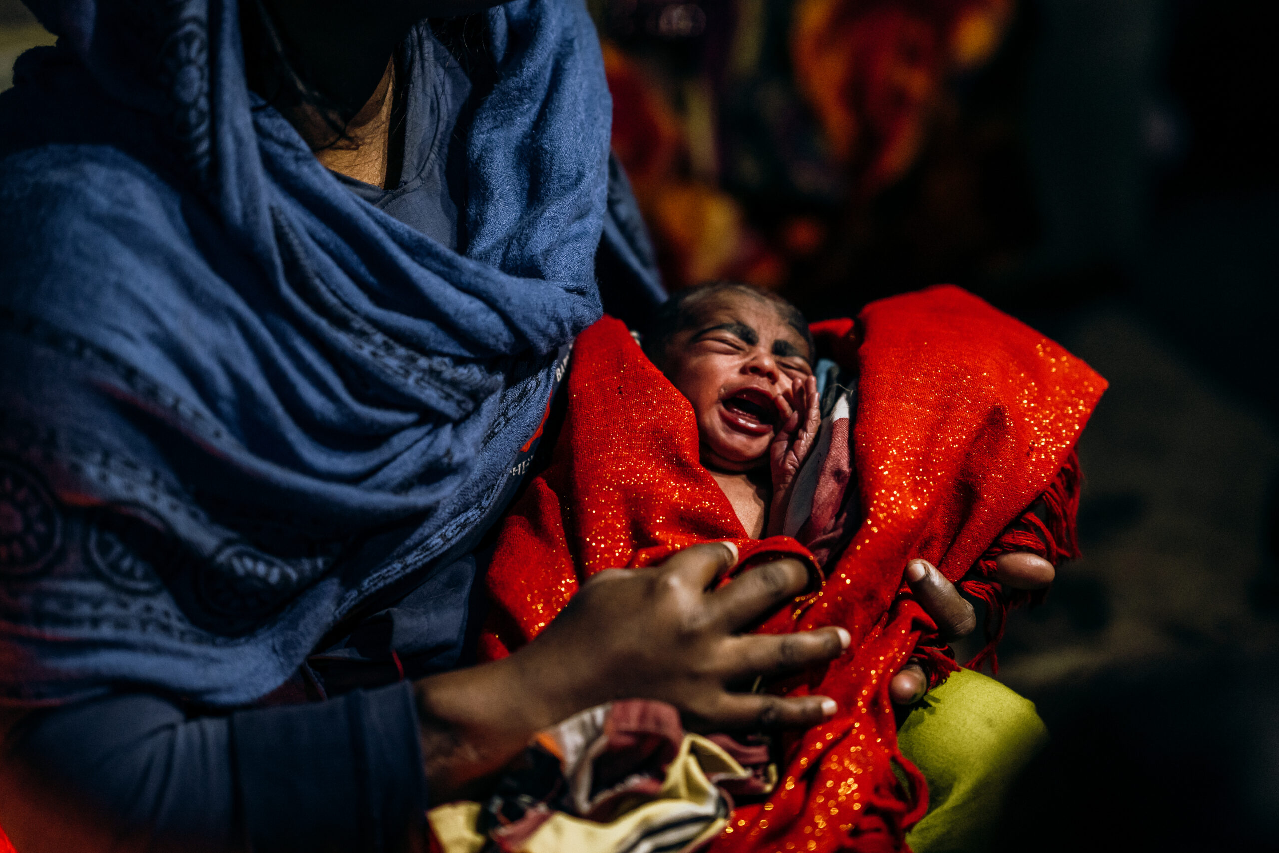 Mother holding crying baby wrapped in a bright red blanket, highlighting urgent need for support during COVID-19 crisis in India.