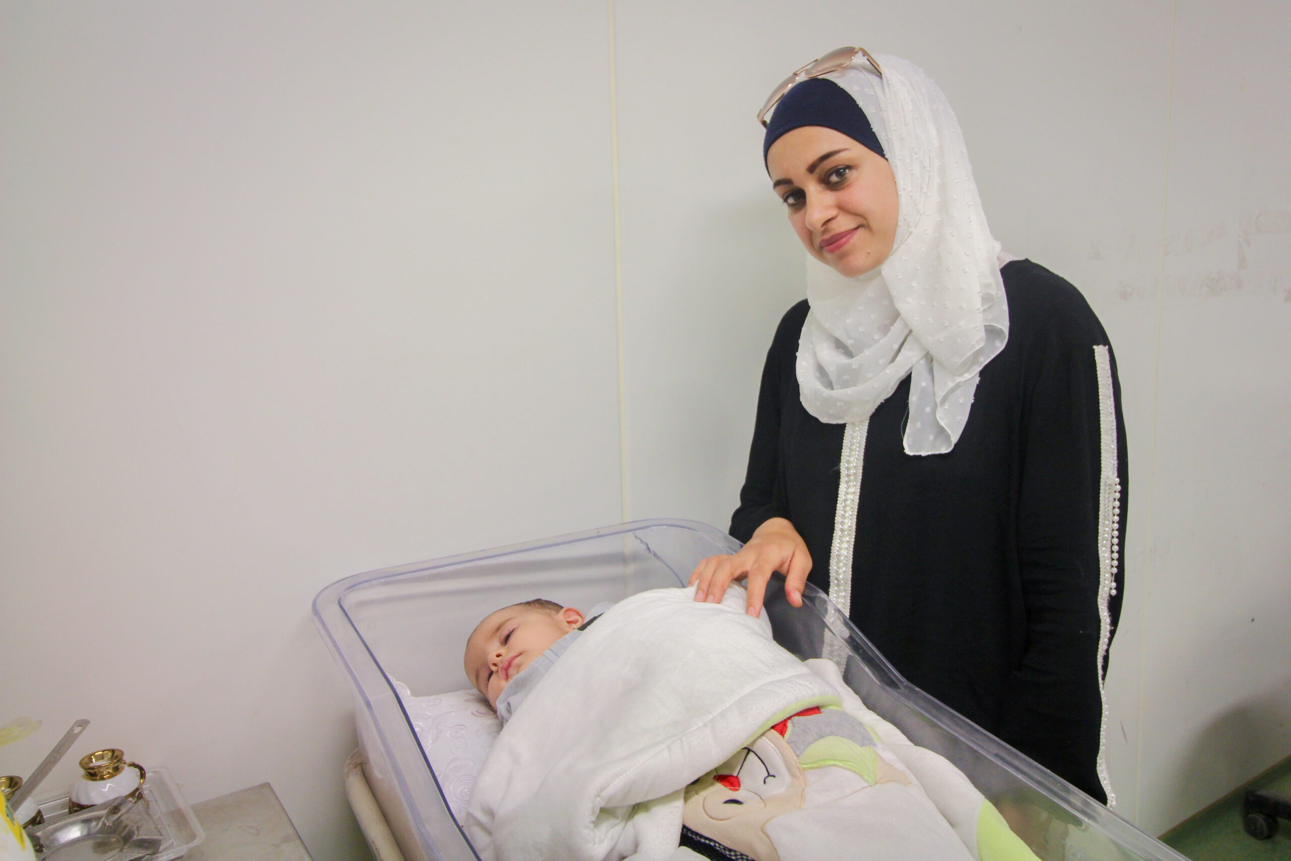 A Syrian mother standing with her baby, who is receiving care in a "hospitainer" Saving Moses provided to help combat high neonatal mortality rates in war zones.