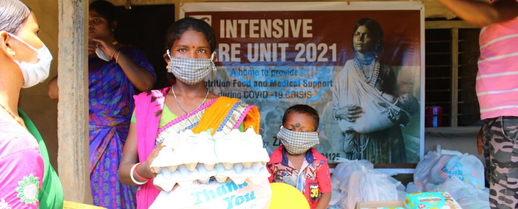 Women and child holding food supplies in front of banner for Intensive Care Unit 2021, providing nutritional food and medical support during COVID-19 crisis.