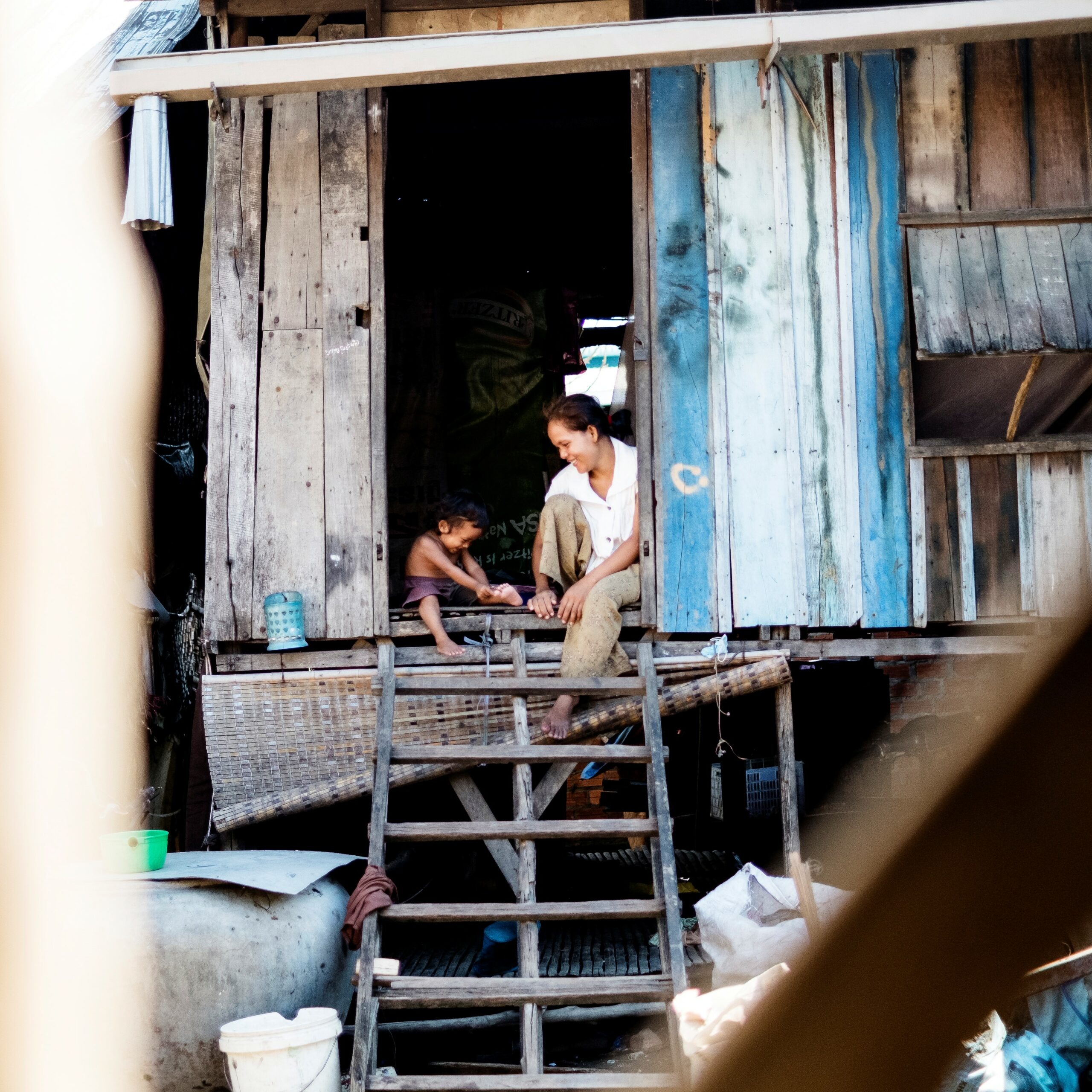 Mother and child sitting on a wooden porch of a makeshift home, engaged in a tender moment, highlighting the need for support for vulnerable families.