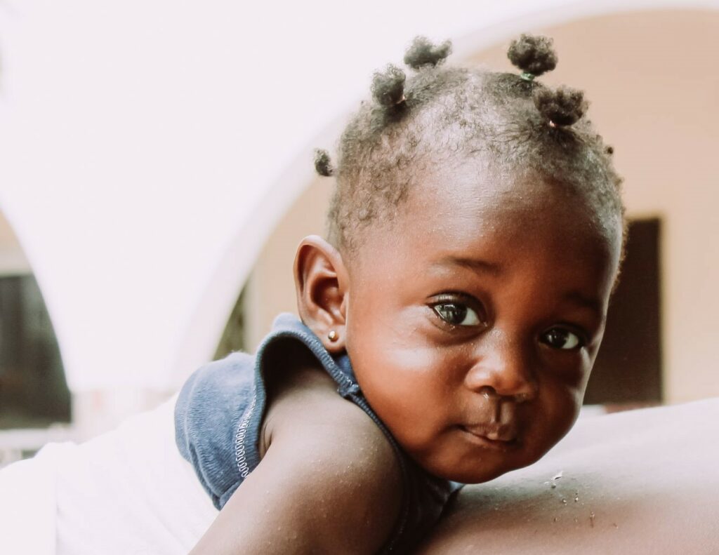 Baby with dark skin and short, curly hair, looking directly at the camera, representing vulnerable children supported by Saving Moses.