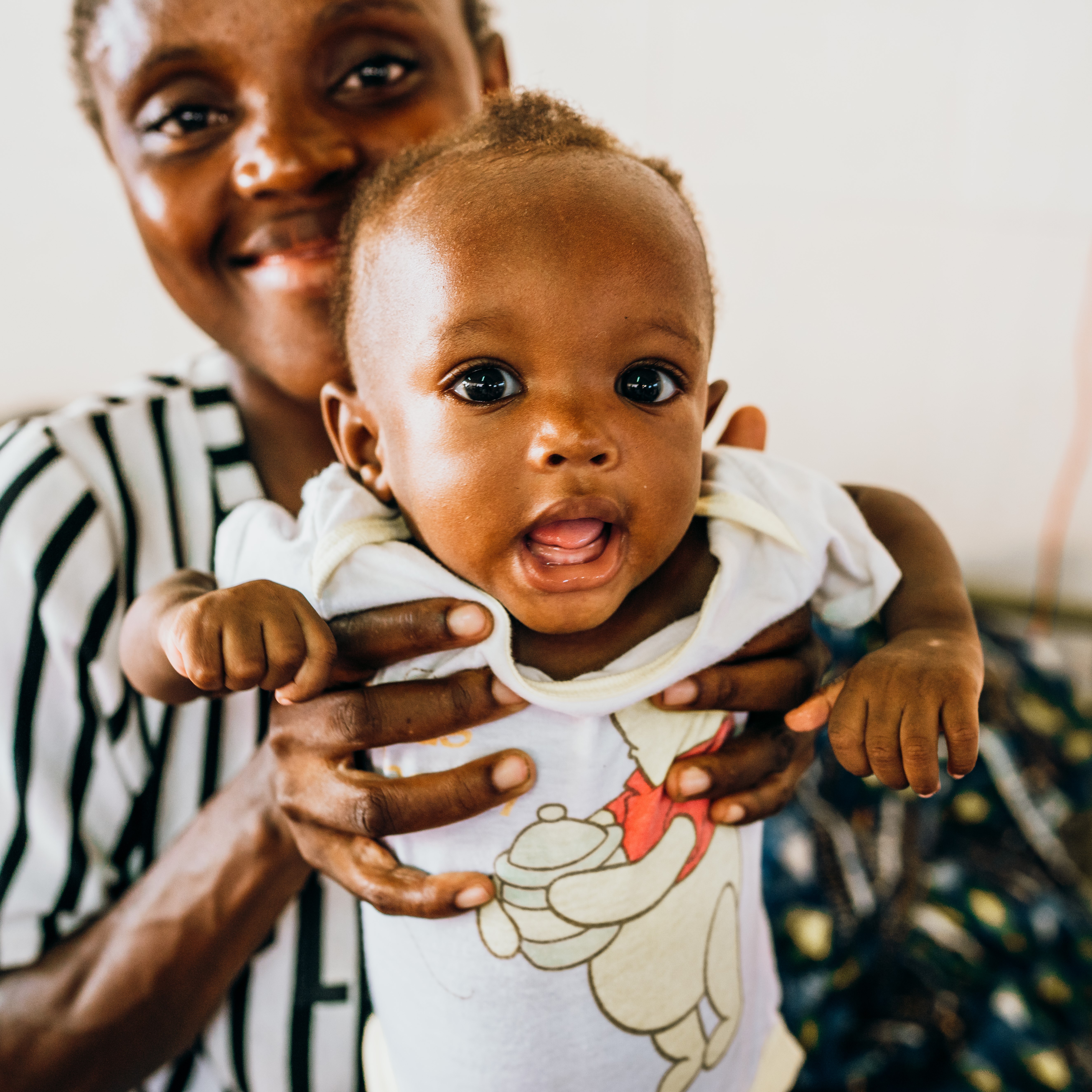 Mother holding smiling baby in a Winnie the Pooh shirt, showcasing the joy of vulnerable children supported by Saving Moses.