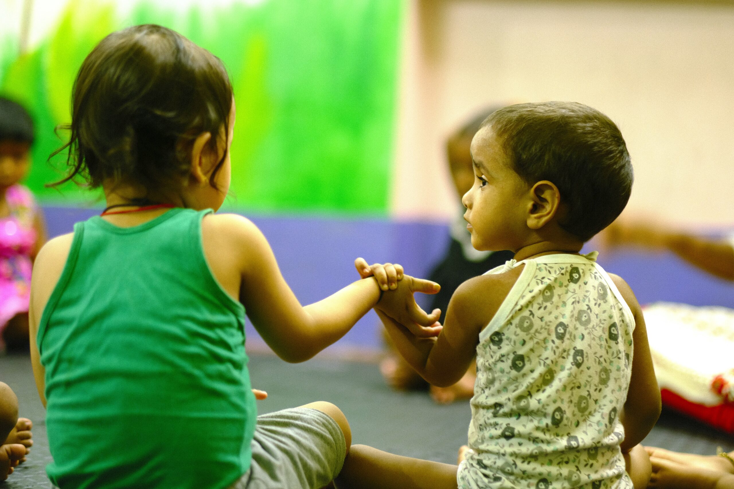 Two young children holding hands, symbolizing connection and support, in a colorful setting, reflecting the mission of Saving Moses to provide life-saving services to vulnerable babies and toddlers.