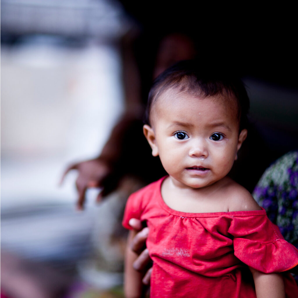 Baby in a red shirt looking directly at the camera, symbolizing hope and vulnerability in the context of Saving Moses' mission to support at-risk infants and toddlers.