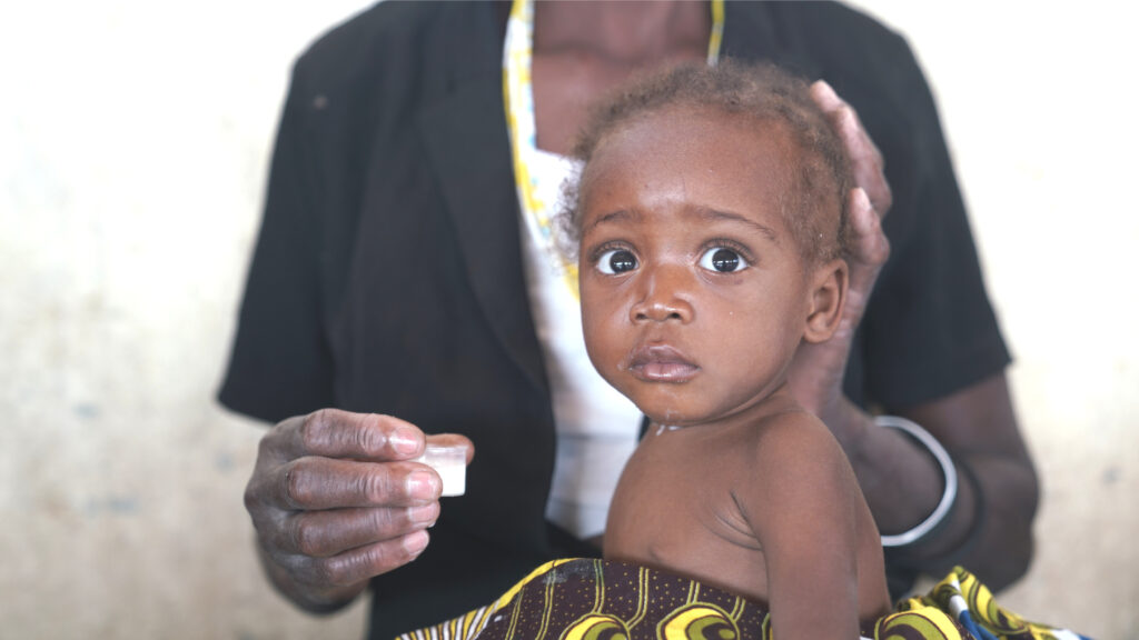 Child receiving therapeutic milk for malnutrition, held by caregiver, in a nurturing environment, supporting Saving Moses' mission to protect vulnerable infants.