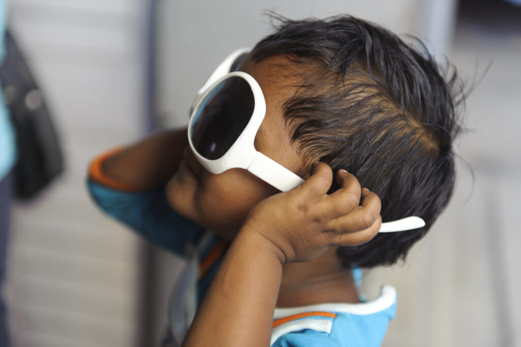 Child wearing oversized white sunglasses, playfully adjusting them, in a context related to Saving Moses's efforts in India to support vulnerable children.