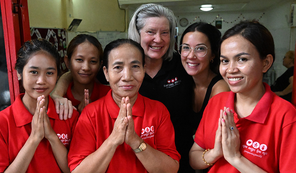 Women in red shirts, including caregivers and staff from Saving Moses, smiling and posing with hands in a prayer gesture, emphasizing compassion and community support for vulnerable children.