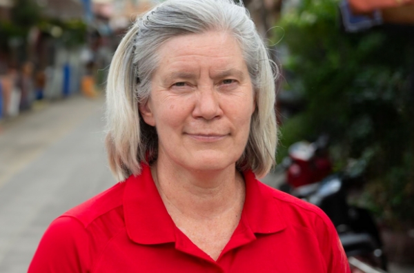 Woman in red shirt, smiling, standing outdoors in a community setting, representing Saving Moses' mission to support babies and toddlers in need.