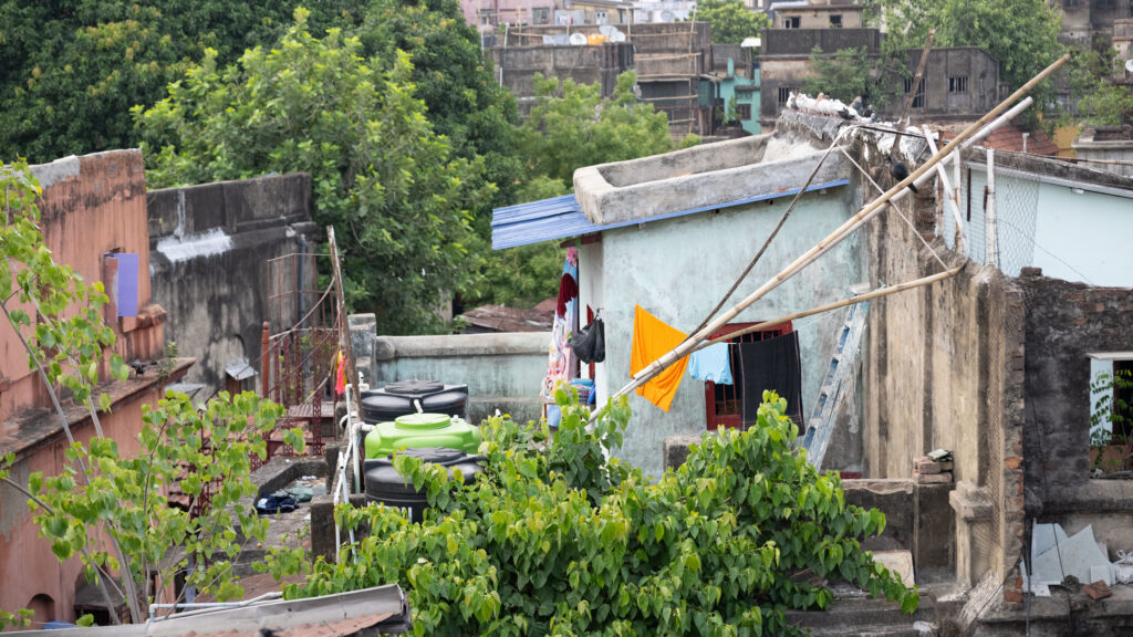 Rooftop view of colorful laundry hanging in Kolkata, India, surrounded by greenery and urban architecture, reflecting the living conditions in the area relevant to Saving Moses's NightCare initiatives.
