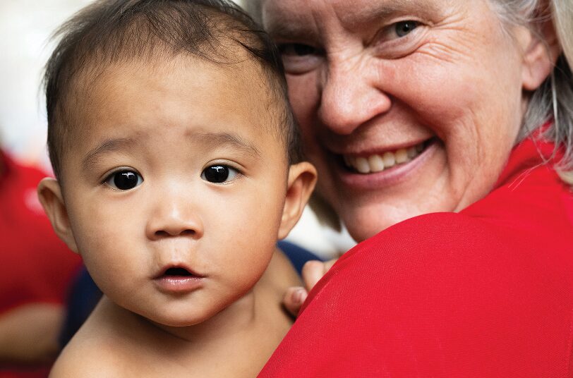 Child with curious expression held by smiling caregiver, both in supportive environment, reflecting Saving Moses' mission to care for vulnerable babies and toddlers.