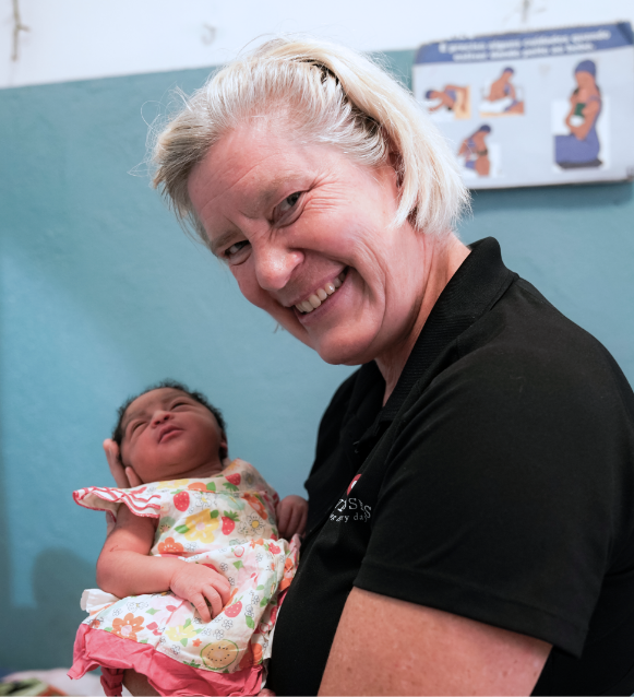 Smiling caregiver holding a newborn baby in a colorful outfit, highlighting maternal support and care in a clinic setting related to Saving Moses' mission for vulnerable mothers and infants.