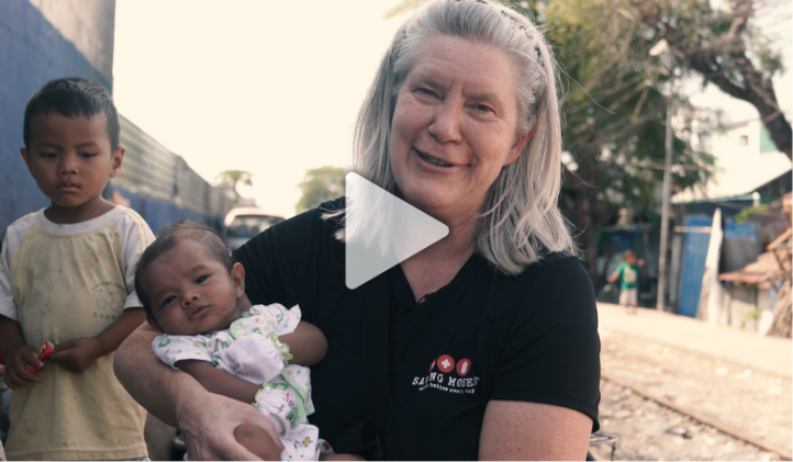 Woman holding a baby, smiling, with a young boy in the background, highlighting Saving Moses' mission to support vulnerable children.