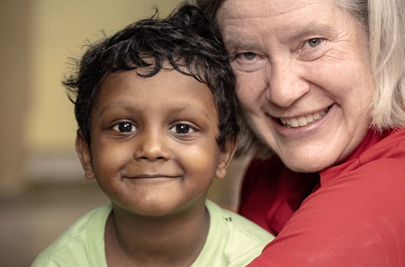 Smiling young boy in green shirt and adult woman with gray hair, both embracing, highlighting care and support for children in Bangladesh.