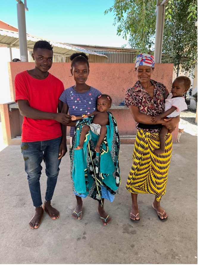 Natalia, 19, holding her baby Lurdish, with her husband Paol, 20, and a woman in traditional attire, outdoors in Angola, representing Saving Moses' humanitarian efforts for vulnerable families.