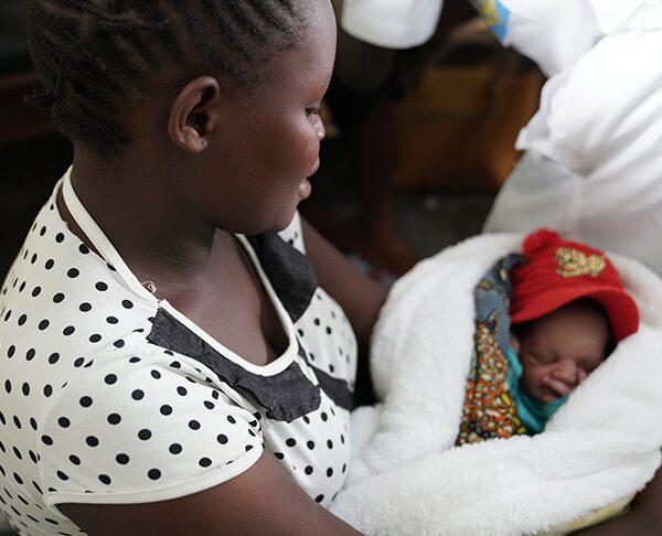 Mother holding a wrapped newborn in a cozy setting, highlighting care and support for vulnerable infants in the DRC.