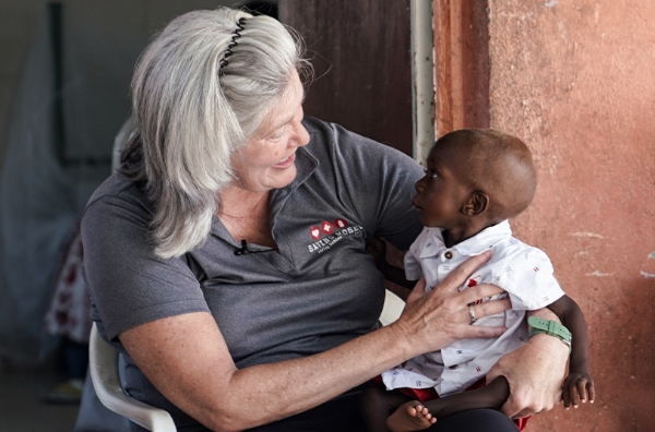 Woman holding and smiling at a malnourished child in a therapeutic setting, highlighting the impact of Saving Moses' support for infants in need.