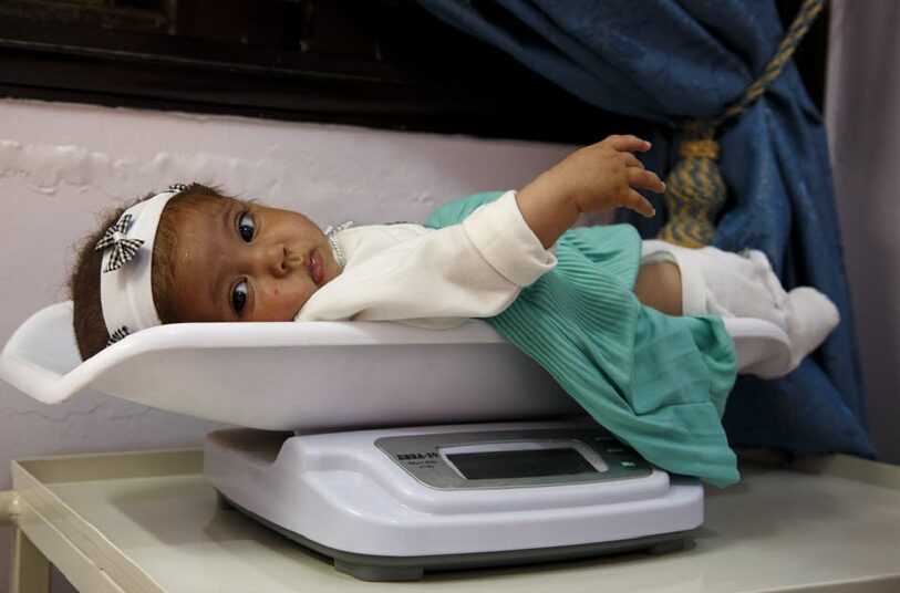 Baby lying on a scale in a clinical setting, emphasizing the importance of health monitoring for infants in support of programs like BirthAid.