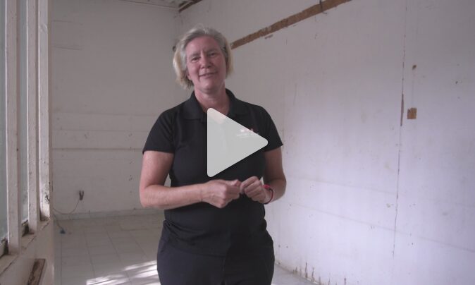 Woman in a black shirt standing in a partially renovated clinic space, emphasizing the transformation of the BirthAid Clinic to support malnourished children and mothers.