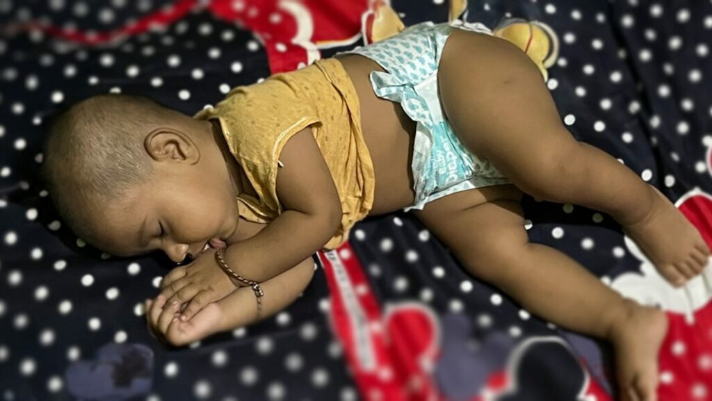 Baby sleeping peacefully on a polka dot blanket, wearing a yellow shirt and diaper, symbolizing safe sleep and care for vulnerable infants.