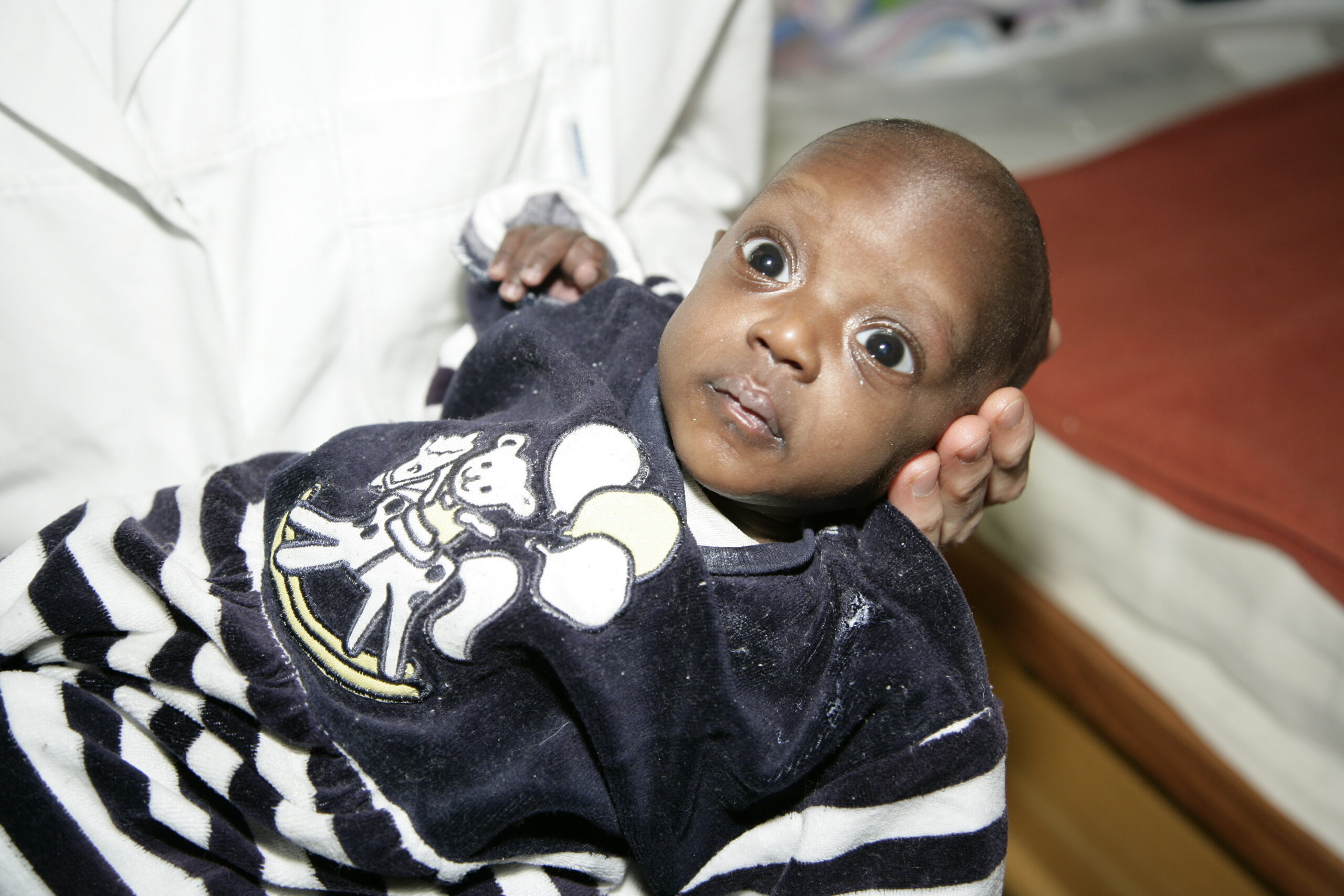 Infant being held, wearing a navy striped outfit with a cartoon character, highlighting the need for safety and care in vulnerable populations.
