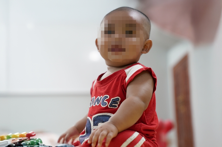 Baby in red shirt sitting on colorful play mat, representing vulnerable infants supported by Saving Moses donations.