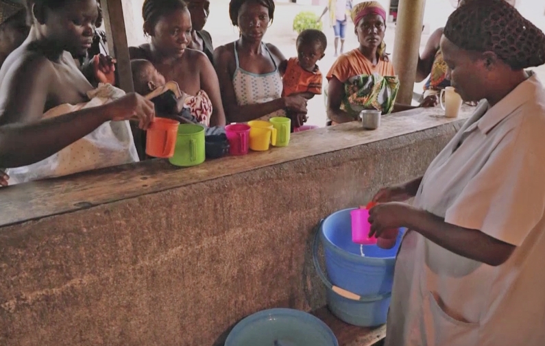 Women receiving nourishment for babies from a caregiver in a community setting, emphasizing the importance of feeding infants at risk of starvation.