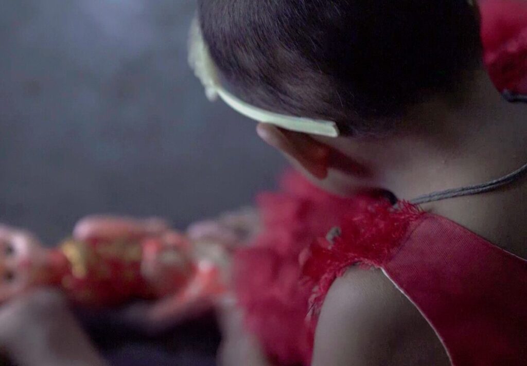 Child in red dress playing with a doll, representing hope and innocence, connected to Saving Moses' mission to support vulnerable babies.